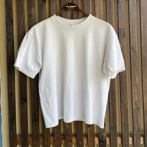 Vit kroppad t-shirt Harvest XL - Vit t-shirt från Harvest Sportswear i 100% bomull. Stor och loose fit med korta ärmar och rund hals men kroppad och sydd för att inte vara för lång. Baksidan har ett färgglatt tryck i blått, rött och gult. Perfekt för dig som gillar retrostil och oversized vibe.