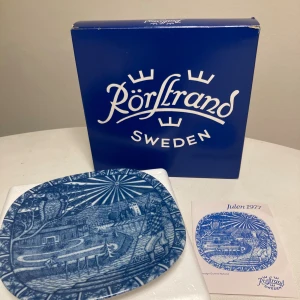 Rörstrand Julen 1977 Samlartallrik - årets julklapp  - Vacker samlartallrik från Rörstrand, Julen 1977, designad av Gunnar Nylund. Tallriken är i blåvitt porslin med detaljerat vintermotiv. Originalkartong och informationsblad medföljer. Tallriken är i mycket fint skick utan synliga skador eller slitage.