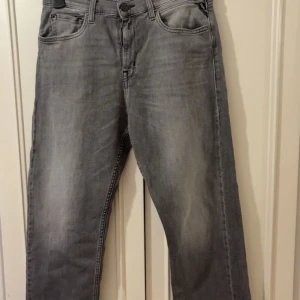Grå jeans från Replay - Säljer ett par grå jeans från Replay med klassisk femficksdesign och snygga detaljer på bakfickorna. Jeansen har en rak passform och är tillverkade i mjukt denimtyg. Perfekta för dig som gillar en stilren och avslappnad look.