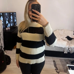 Randig stickad tröja i svart och vitt - Säljer en snygg stickad tröja med breda svarta och vita ränder. Tröjan har rund hals, lång ärm och ribbade muddar. Modellen är normal i passningen och har en liten slits på sidorna för extra komfort. Perfekt för dig som gillar klassisk streetstyle.