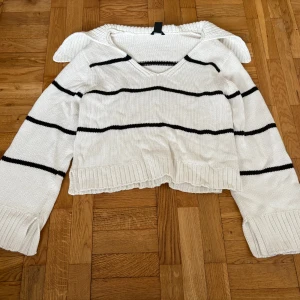 Vit stickad randig tröja Lindex S - Vit stickad tröja från Lindex i storlek S med svarta horisontella ränder. Tröjan har v-ringning, breda muddar och en lite croppad passform. Perfekt för lager-på-lager och chill vibes.