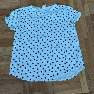 Vit prickig t-shirt från Zara - Vit t-shirt från Zara med svarta prickar över hela plagget. Klassisk rund halsringning och korta ärmar. Tillverkad i mjuk bomull, perfekt för en avslappnad och trendig look.