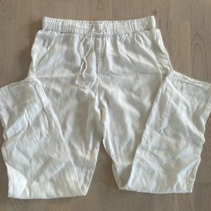 Vita linnebyxor från H&M HOME - Säljer ett par vita linnebyxor från H&M HOME med avslappnad passform och elastisk midja med snörning. Byxorna är raka i modellen och tillverkade i svalt linnematerial, perfekta för chill dagar eller när du vill ha en clean look.