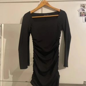 Svart långärmad klänning från SHEIN - Svart kortklänning från SHEIN med lång ärm och fyrkantig urringning. Klänningen har snygg rynkdetalj längs sidorna och ryggen som ger en tight och smickrande passform. Perfekt för dig som gillar stilrena och trendiga plagg.