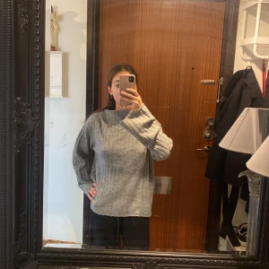 Grå ribbstickad tröja från 157 - Mysig grå ribbstickad tröja från 157 med rak passform och högre hals. Tröjan har långa ärmar och är perfekt för lager-på-lager. Enkel och stilren design som funkar till många outfits.