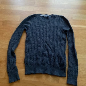 Mörkgrå stickad tröja från Gina Tricot - Mysig mörkgrå stickad tröja från Gina Tricot med kabelstickat mönster. Tröjan har rund halsringning och långa ärmar. 