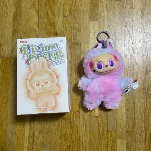 Pop Mart Big Onto Energy Plush Keychain - Söt Pop Mart Big Onto Energy plush-figur med lila och rosa päls, komplett med originalförpackning. Perfekt som samlarobjekt eller dekoration. Produkten ser ut att vara i nyskick utan synligt slitage eller defekter. Passar utmärkt som present till fans av designerleksaker.