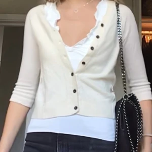 Vit kofta med knappar - Snygg vit kofta med svarta knappar och trekvartsärm. Perfekt att slänga över ett linne eller topp för en fräsch och stilren look. Koftan är i mjukt material och har en klassisk passform som funkar till det mesta.