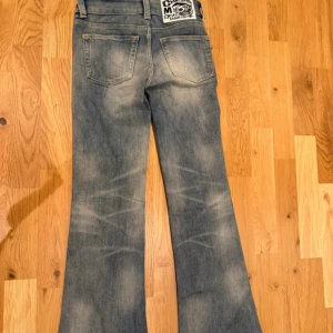 Bootcut jeans från MONDAY, ljusblå - Bootcut jeans från MONDAY i ljusblå tvätt med slitningar och klassiska fem fickor. Byxorna har låg midja och är tillverkade i en stretchig bomullsblandning för skön passform. Perfekta för dig som gillar retrovibbar och snygg siluett.