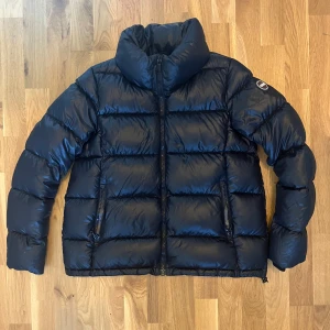 Svart/mörkblå pufferjacka från Colmar - Säljer en svart pufferjacka från Colmar. Jackan är dunfylld och har en clean, stilren look med Colmar-logga på ärmen. Perfekt för vintern, vid kalla dagar. Skriv vid funderingar !