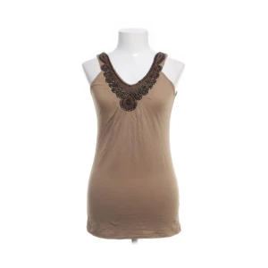 Beige linnetopp med pärldetaljer - Snygg beige linnetopp med djup v-ringning och dekorativa pärldetaljer i brunt och svart längs halsringningen. Toppen är ärmlös och har en smickrande passform som passar perfekt till sommaren.