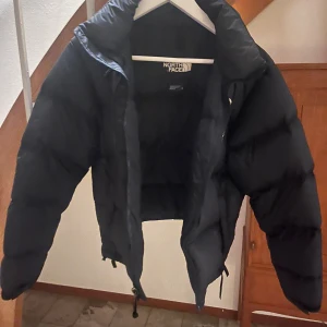 Svart pufferjacka från The North Face XS - Säljer en svart pufferjacka från The North Face i storlek XS. Jackan har hög krage, dragkedja framtill och två sidofickor med dragkedja. Klassisk logga på bröstet och justerbar dragsko nertill. Perfekt för kalla dagar.