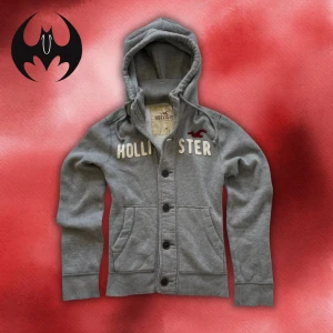 Grå hoodie / cardigan med knappar från Hollister M/L - Grå hoodie / cardigan från Hollister med knappar och broderad logga och text på bröstet | M/L | Vintage och extremt limiterad! | Längd: 65cm Axelbredd: 40cm Armlängd: 70cm