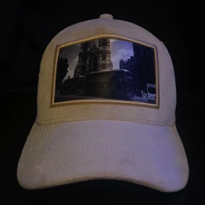 Beige keps från Sayless med fototryck - Snygg beige keps från Sayless med ett unikt fototryck framtill som visar en stadsmiljö med bussar och byggnader. Kepsen har en böjd skärm och är tillverkad i ett mjukt material med mesh på insidan för extra komfort. Perfekt accessoar för en cool streetstyle.