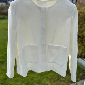 Vit kavaj från H&M, storlek 42 - Stilren vit kavaj från H&M i storlek 42. Jackan har rund halsringning, två stora fickor framtill och dold knäppning. Materialet är strukturerat och ger en clean look. Perfekt för dig som gillar minimalistisk stil.