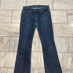 Bootcut jeans från 7 For All Mankind - Snygga blå bootcut jeans från 7 For All Mankind med klassisk femficksdesign och guldfärgade detaljer. Jeansen har normal passform och är tillverkade i slitstarkt denimtyg. Perfekta för dig som gillar en tidlös look med lite utsvängda ben.