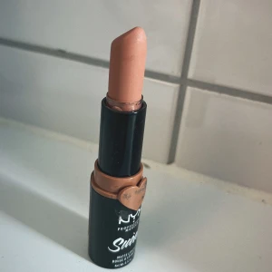 NYX Suede Matte Läppstift Nude - NYX Suede Matte Lipstick i en snygg nude/ljusbeige nyans. Läppstiftet har en matt finish och kommer i en svart hylsa med ett hjärta i samma färg som stiftet. 