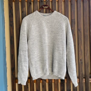 Ljusgrå stickad tröja i akryl - En enkel och stilren ljusgrå stickad tröja från Acryl Highbulk. Tröjan har rund halsringning, lång ärm och är tillverkad i mjukt akrylmaterial. Perfekt för lager-på-lager, finmiddag eller till många olika outfits.