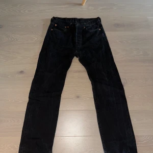 Svarta Levi's 501 jeans W31 L32 - Svarta Levi's 501 jeans med klassisk rak passform och knappgylf. Jeansen har fem fickor och den ikoniska läderpatchen bak i midjan. Perfekta för dig som gillar en tidlös och clean look.