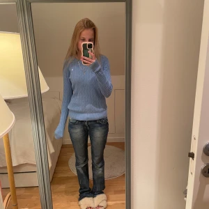 Ljusblå kabelstickad tröja - Supersnygg ljusblå kabelstickad tröja med liten vit broderad logga på bröstet. Tröjan har rund hals, ribbade muddar och lång ärm. Perfekt till jeans och smycken för en clean look.