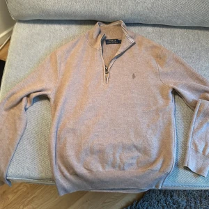 Beige stickad tröja Polo Ralph Lauren - Säljer en snygg beige stickad tröja från Polo Ralph Lauren med halv dragkedja och broderad logga på bröstet. Tröjan har lång ärm, ribbade muddar och klassisk passform. Perfekt för lager-på-lager under höst och vinter.