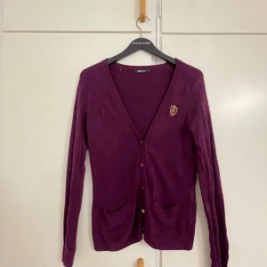 Vinröd kofta från Gina Tricot XS - Vinröd kofta från Gina Tricot i storlek XS. Koftan har v-ringning, knappar framtill, två fickor och en liten broderad detalj på bröstet. Långärmad och i mjukt material, perfekt för lager-på-lager under hösten.