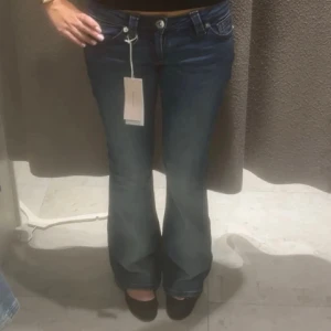 Gin Tricot bootcut jeans med röd söm - Mörkblå bootcut jeans från Gina Tricot med snygga röda sömmar på bakfickorna. Låg midja och klassisk femficksmodell. Jeansen har en lätt utsvängd passform nertill och är tillverkade i mjukt denimtyg för en bekväm känsla.
