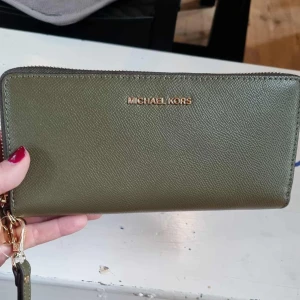 Olivgrön plånbok Michael Kors - Snygg olivgrön plånbok från Michael Kors i skinn med guldfärgade detaljer och dragkedja. Plånboken har flera kortfack, myntfack med dragkedja och plats för sedlar. 💖
