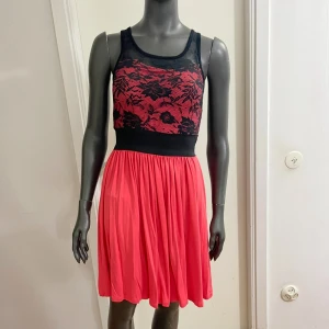 Svart och röd spetsklänning från Dochka - Snygg kort klänning från Dochka med svart spets upptill och röd kjol. Överdelen har blommigt spetsmönster och är ärmlös med rund halsringning. Midjan är markerad med bred svart resår och kjolen är lätt utställd. Perfekt för dig som vill sticka ut!