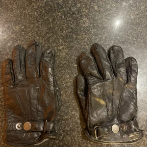 Svarta skinnhandskar från Hestra - Säljer ett par svarta skinnhandskar från Hestra i storlek 8. Handskarna har snygga detaljer med tryckknappar och justerbart band vid handleden. Insidan är fodrad med mjukt stickat material som däremot är ganska slitna. Kostar 1200kr nya men är ganska slitna. Perfekt för höst och vinter!