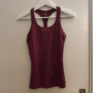 Vinröd träningstopp från H&M - Säljer en vinröd linnetopp från H&M med brottarrygg. Toppen är figurnära och tillverkad i ett stretchigt syntetmaterial som passar perfekt för träning. Enkel och stilren design utan mönster eller extra detaljer.