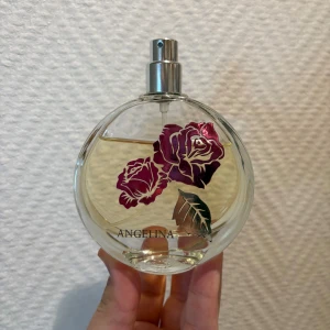 Angelina parfym med rosdesign - Snygg parfym med rosor på flaskan och namnet Angelina. Perfekt för dig som vill ha en stilren accessoar på hyllan och även lukta gott! Den har använts några gånger men nästan hela flaskan är full fortfarande! Tyvärr är locket borttappat. 