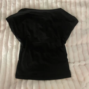 Svart topp med öppen rygg - Snygg svart topp med korta ärmar och en stor öppen rygg. Modellen är croppad och har en enkel, stilren design som passar perfekt till jeans eller kjol. Tunt och mjukt material som känns skönt mot huden.