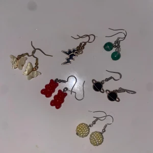 Mixade örhängen med coola motiv - Sex par örhängen med olika motiv: fjärilar i pärlemor, svarta blixtar, gröna kulor, röda nallebjörnar, svarta planeter och ljusgula bollar med pärlor. Perfekt för dig som vill variera din stil och sticka ut med färg och form.