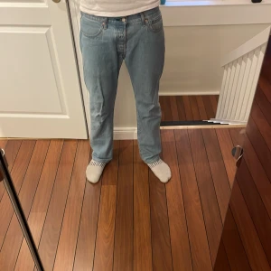 Levi's 501 ljusblå jeans W33 L30 - Klassiska Levi's 501 jeans i ljusblå denim. Rak passform med normal midja och femficksdesign. Ikonisk läderpatch bak och röd Levi's-tagg på bakfickan. Perfekta för en avslappnad och tidlös look.