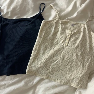 2 linnen från Brandy Melville - Säljer två linnen från Brandy Melville. Ett marinblått ribbat linne med smala axelband och ett cremevitt linne med små blommor, knappar framtill och tunna axelband. Båda är i mjuk bomullsblandning och perfekta för sommaren.