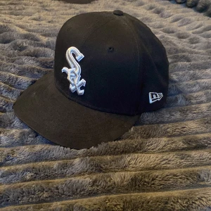 Svart New Era keps White Sox - Svart keps från New Era med broderad vit White Sox-logga framtill och New Era-logga på sidan. Klassisk böjd skärm och strukturerad passform. Tillverkad i 100% bomull för en bekväm känsla. Perfekt för dig som gillar sportig streetstyle.