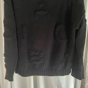 Svart stickad tröja från ONLY XS - Svart stickad tröja från ONLY i storlek XS. Tröjan har coola upphöjda detaljer i samma färg och ribbade muddar vid ärmslut och nederkant. Perfekt för dig som gillar en enkel men ändå unik look.