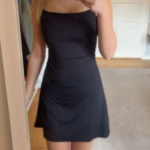 Svart glittrig kort klänning H&M Divided - Supersnygg svart kort klänning från H&M Divided med tunna axelband och diskret glittrigt tyg. Enkel och stilren modell som sitter slimmat över kroppen och har en rak halsringning. Perfekt för dig som gillar minimalistisk men ändå festlig stil. Aldrig använd