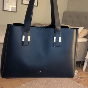 Svart väska - Stilren svart handväska i skinn från Zalando (Anna Field) med raka linjer, dubbla handtag och snygga gulddetaljer. Väskan har 3 stora fack, varav ett med dragkedja. Det mittersta facket med dragkedja är avtagbart så man kan få ett stort fack. Klassisk och rymlig modell som funkar till allt och är bra att ha. (Väskan är helt ny och har aldrig varit utanför mitt rum därav priset.)