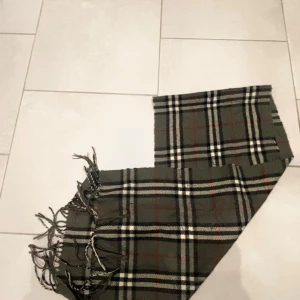 Rutig halsduk från Burberry - Klassisk rutig halsduk från Burberrys i 100% lammull.  Halsduken har fransar i ändarna och den ikoniska Burberry-rutan. Perfekt accessoar för att lyfta din outfit.