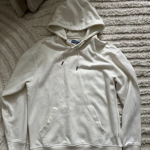 Vit hoodie från Blend - Säljer en stilren vit hoodie från Blend med klassisk huva och dragsnören. Tröjan har en stor magficka och långa ärmar med ribbade muddar. Perfekt för dig som gillar en enkel och clean look.
