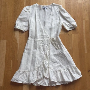 Fin vit omlottklänning från & Other Stories - Superfin vit omlottklänning från & Other Stories med volangkant nertill och puffiga korta ärmar. Klänningen har knyt i midjan och v-ringning, tillverkad i ett lätt och luftigt tyg som passar perfekt till varma dagar. I fint skick!