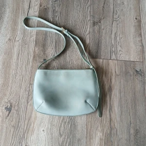 Ljusgrön axelväska i skinn - Snygg ljusgrön axelväska i slätt skinn med minimalistisk design. Väskan har justerbar rem och stängs med dragkedja upptill. Perfekt för dig som gillar stilrena accessoarer med en modern touch.