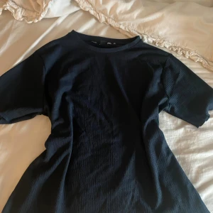 Svart ribbad t-shirt från 157 XS - En svart ribbad t-shirt från 157 i storlek XS. T-shirten har korta ärmar, rund halsringning och är tillverkad i ett mjukt, stretchigt material som sitter snyggt på kroppen. Perfekt basic-plagg med enkel och stilren look.