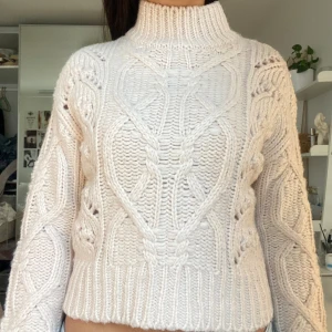 Vit stickad polotröja med kabelmönster - Säljer en chunky vit stickad polotröja med grovt kabelstickat mönster och hög krage. Tröjan har en loose fit och långa ärmar, perfekt för kyliga dagar. Supermysig och lätt att styla med jeans eller kjol.
