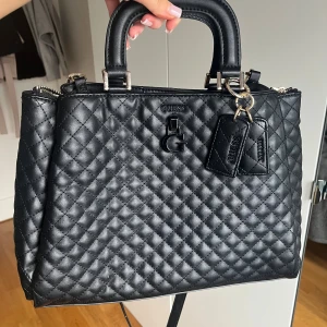 Guess svart väska  - Säljer den här svarta guess väskan för den aldrig kommer till användning. 3 stor fack sen fler små fack