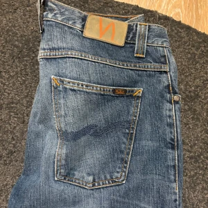 Blå Nudie Jeans med slitna knän - Säljer ett par klassiska blå jeans från Nudie Jeans med snyggt slitna detaljer och trasiga knän. Jeansen har raka ben, fem fickor och orangea sömmar. Modellen heter straight sven och går ej att få tag i nå mer. Storlek 32/36.