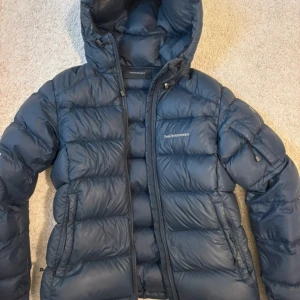 Mörkblå dunjacka Peak Performance S - Peak Performance dunjacka i mörkblått med huva och dragkedja. Nypris 4000kr. Två små hål som inte märks💗🥂🍾☀️