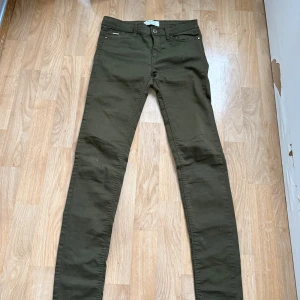 Mörkgröna skinny jeans Stradivarius - Snygga mörkgröna skinny jeans från Stradivarius i storlek 34. Klassisk femficksmodell med dragkedja och knapp framtill. Jeansen har en tight passform och är tillverkade i ett mjukt bomullsmaterial med lite stretch för extra komfort.
